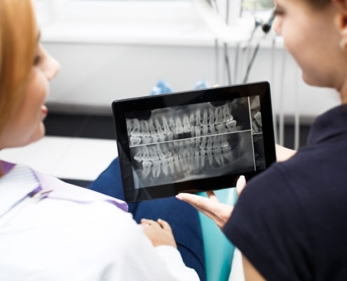 A dental professional shows a patient a dental X-ray image on a tablet during a consultation.