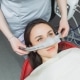 A dental patient reclines in a chair while a dental professional places a nitrous oxide sedation mask over her nose.